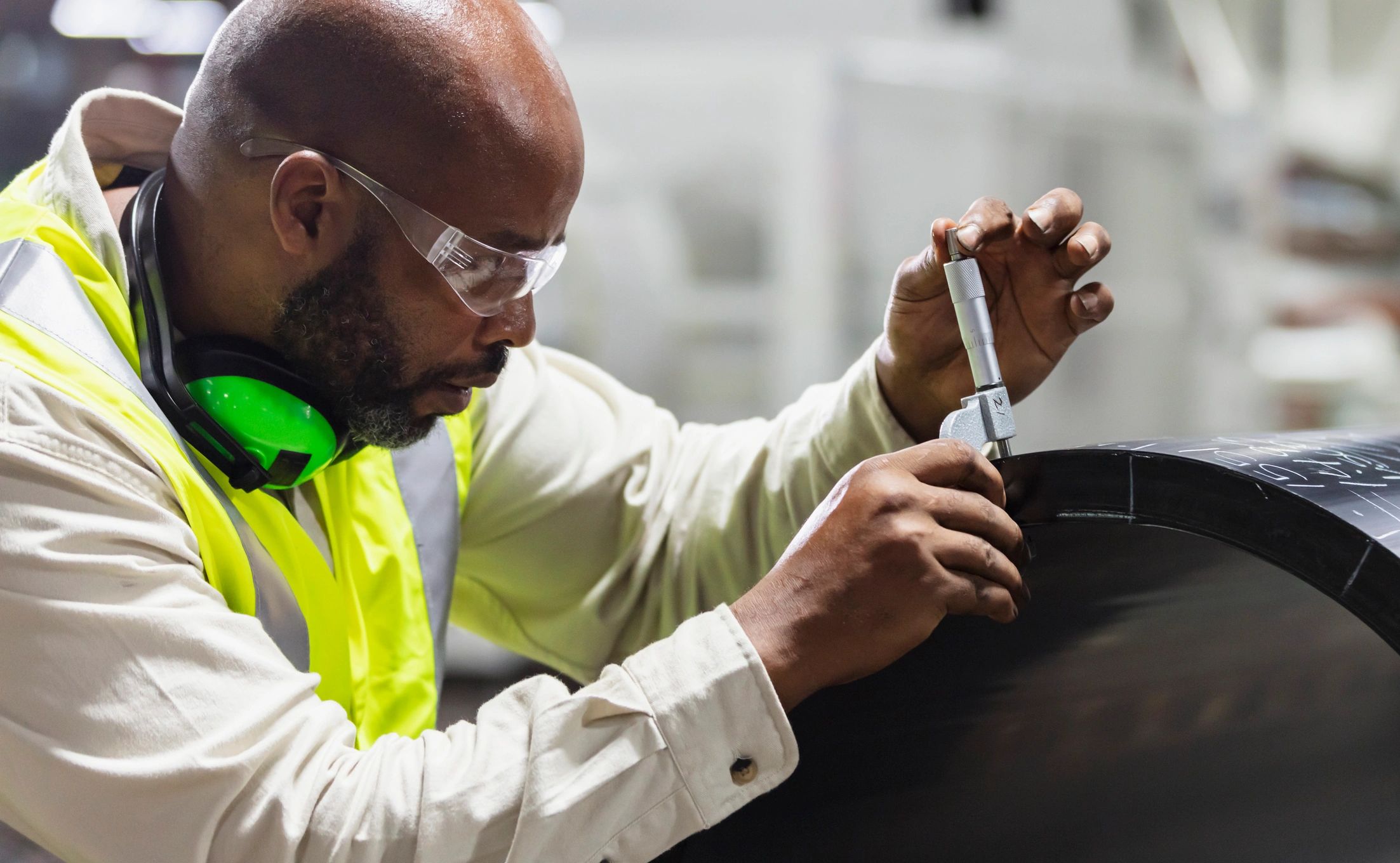 Inspector measuring thickness on a manufactured cylinder in a factory